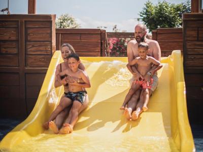 Two people slide down a yellow water slide into a pool on a sunny day.