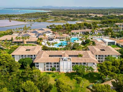 Large hotel complex with multiple buildings, pool, and tennis courts surrounded by greenery.
