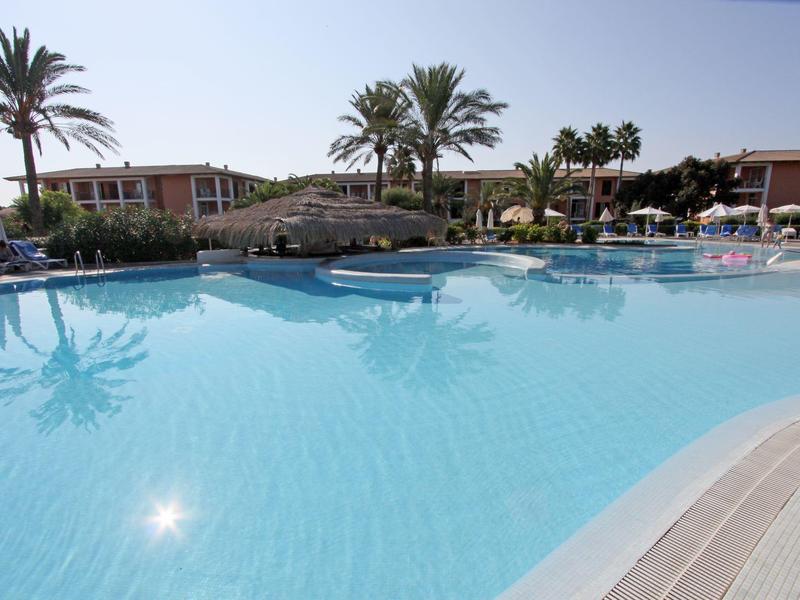 Large hotel pool with palm trees and sun loungers on a sunny day