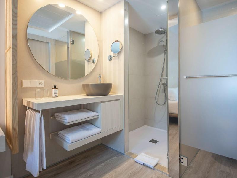 Modern bathroom with round mirror, sink, and walk-in shower in a light design.