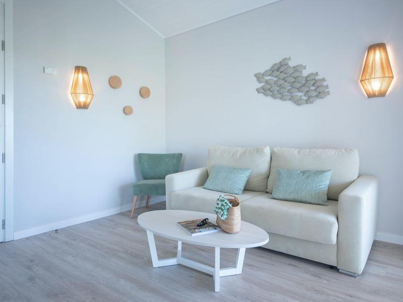 Bright modern living room with sofa, green armchair, table, and decorative wall lamps.