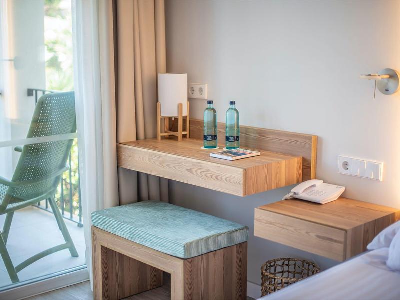 Bright hotel room with desk, stool, balcony, and outdoor view.