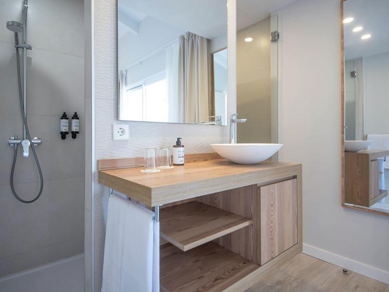Modern hotel bathroom with wooden vanity, round sink, and walk-in shower.