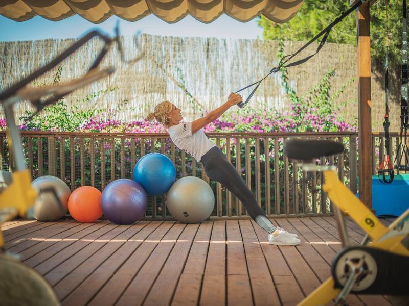 A child swings on a rope in a wooden outdoor area with balls and toys.