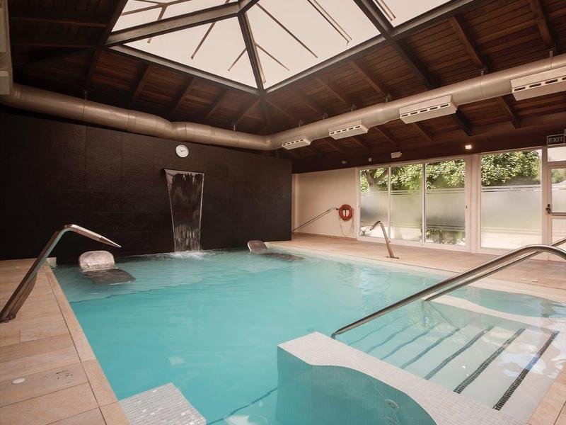 Interior space with swimming pool, wooden ceiling, and large windows letting in natural light.