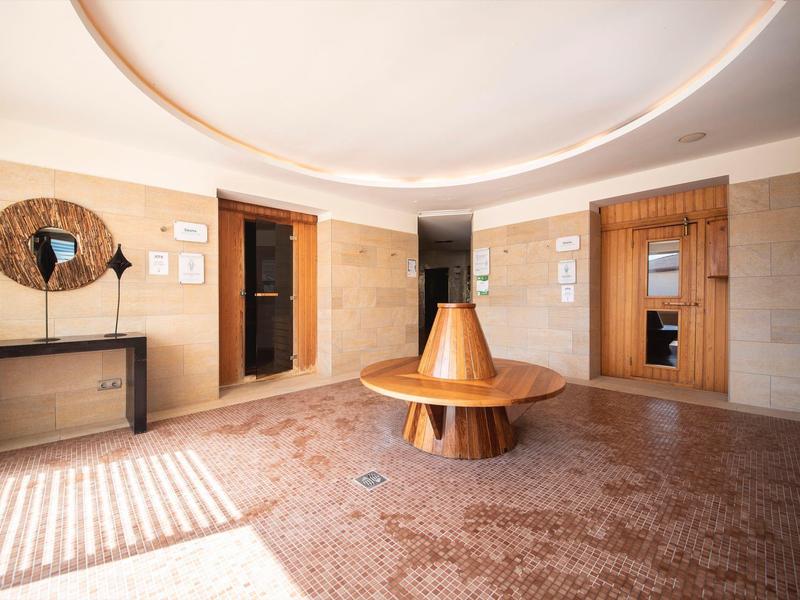 Bright hotel lobby with round wooden table, mirror, and elevator doors.