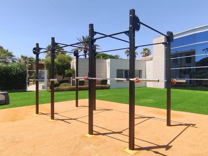 Modern outdoor fitness area with pull-up bars and loungers in front of glass building under clear sky.