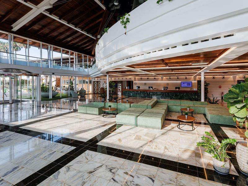 Bright, modern hotel lounge area with green sofas and marble tile flooring.