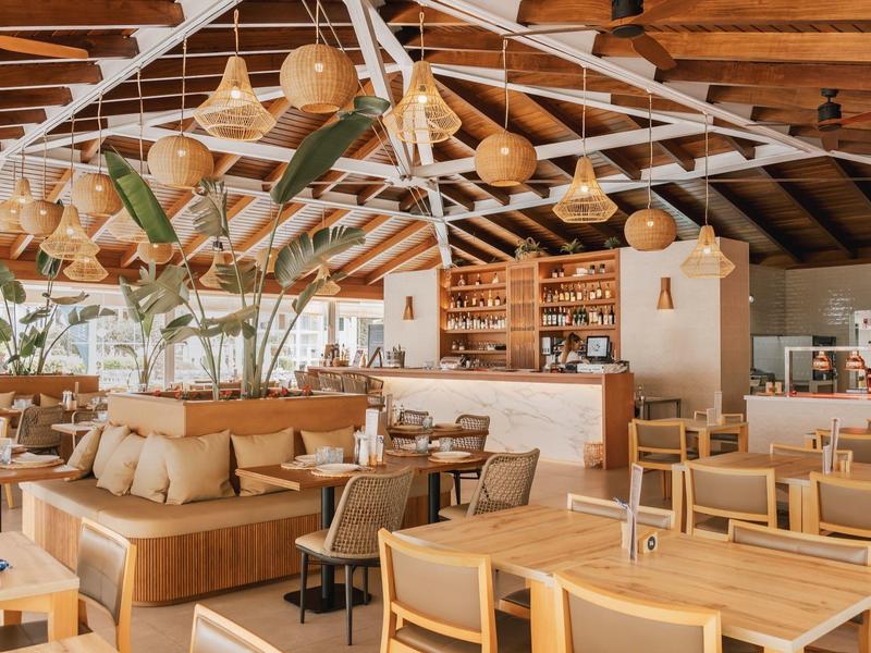 Bright restaurant with wooden furniture, plants, and modern design under a beam ceiling.