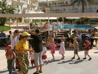 Kinder stehen in einer Schlange im Freien vor einem Hotel mit Pool und Palmen.