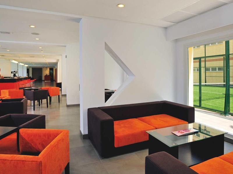 Modern lounge with orange and black sofas and view of a tennis court.