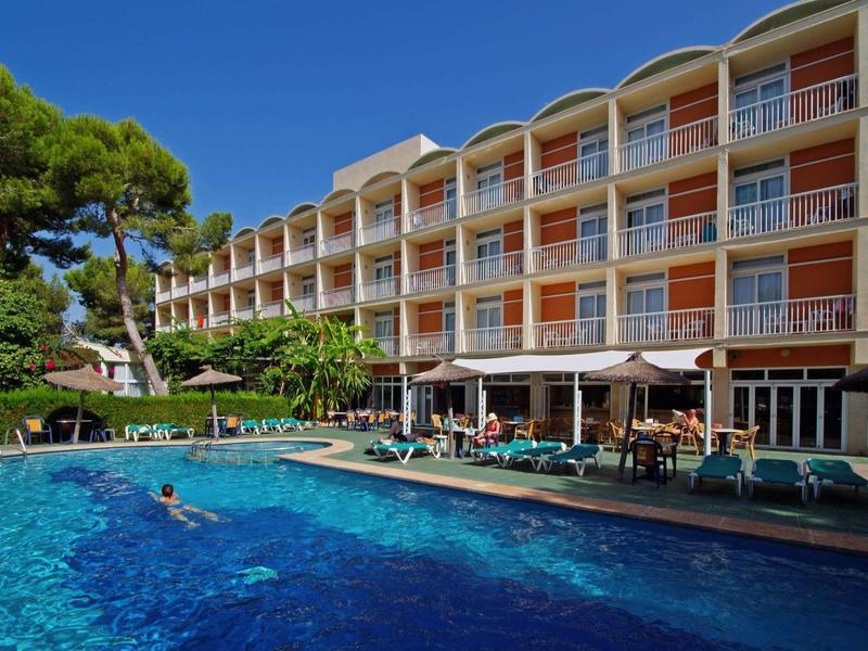 Four-story hotel with terrace and outdoor pool in a sunny setting.