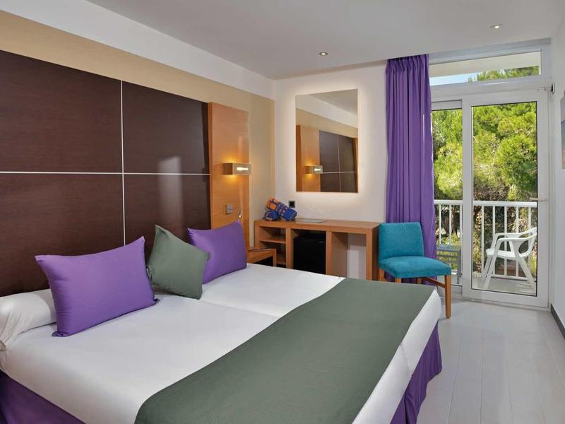Modern hotel room with double bed, purple curtains, and balcony with green view.