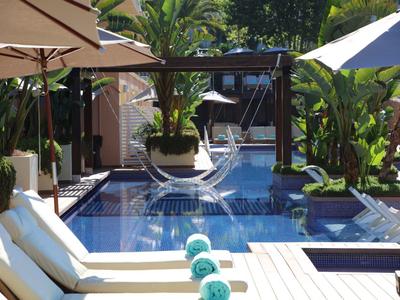 Poolbereich mit Sonnenliegen, großen Schirmen, Palmen und modernen Sitzgelegenheiten in hellem Licht.