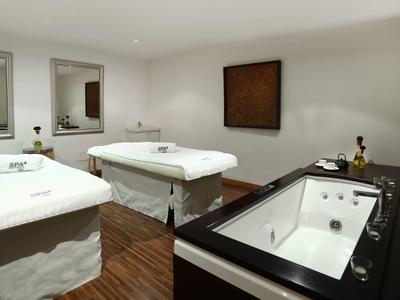 Moderner Spa-Raum mit zwei Massageliegen und einem großen Whirlpool, holzfarbener Boden.