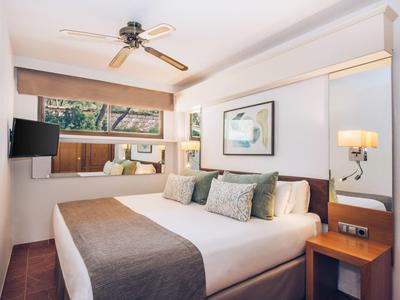 Gemütliches Schlafzimmer mit Doppelbett, Kissen, Deckenventilator und großem Fenster mit Blick.