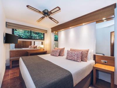 Modernes Schlafzimmer mit großem Bett, Deckenventilator, Holzmöbeln und Fenster mit Außenblick.