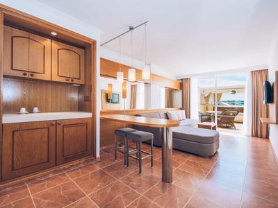 Helles Wohnzimmer mit Holzmöbeln, Stehtisch, Hocker, Sofa und großem Fenster mit Blick auf Terrasse.