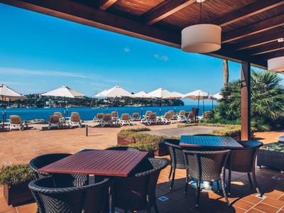 Terrassenbereich mit Stühlen, Tischen und Sonnenschirmen am Strand unter blauem Himmel.