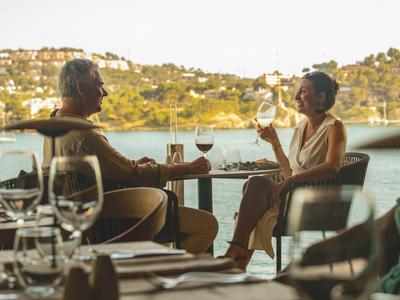 Due persone che si godono bevande su una terrazza con vista su un lago e colline.