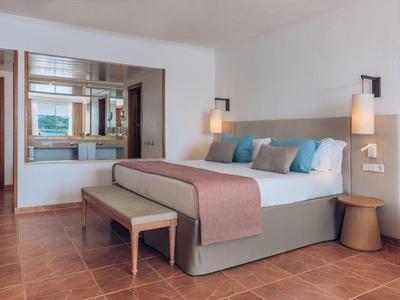 Hell eingerichtetes Schlafzimmer mit großem Bett, zwei Hängelampen, Holzboden und Fensterblick.