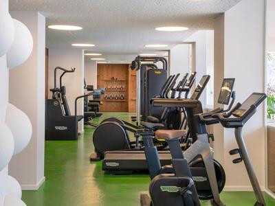 Moderner Fitnessraum mit verschiedenen Trainingsgeräten und grünem Bodenbelag in einem Hotel.