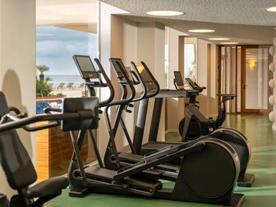 Moderner Fitnessraum mit Steppern und Blick auf das Meer durch große Fenster.