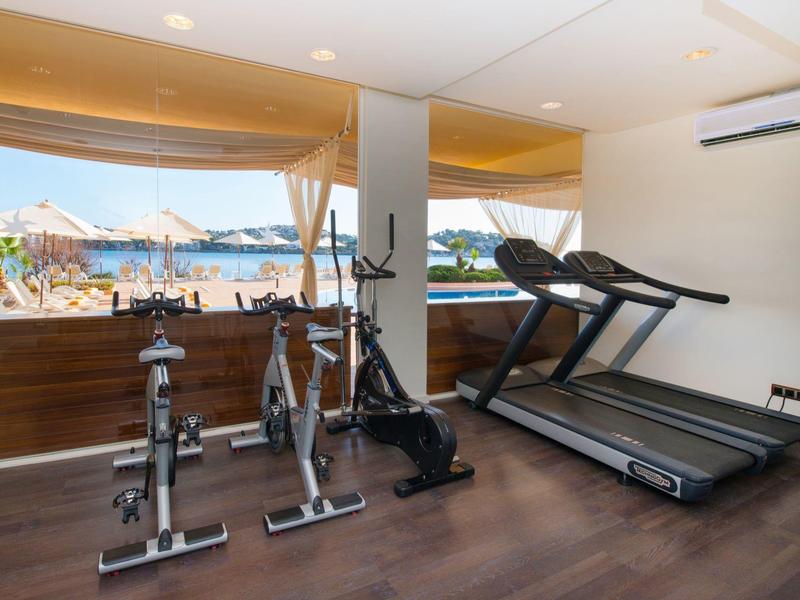 Fitnessraum mit zwei Spinning-Bikes, einem Heimtrainer und zwei Laufbändern, helle Fensterfront.