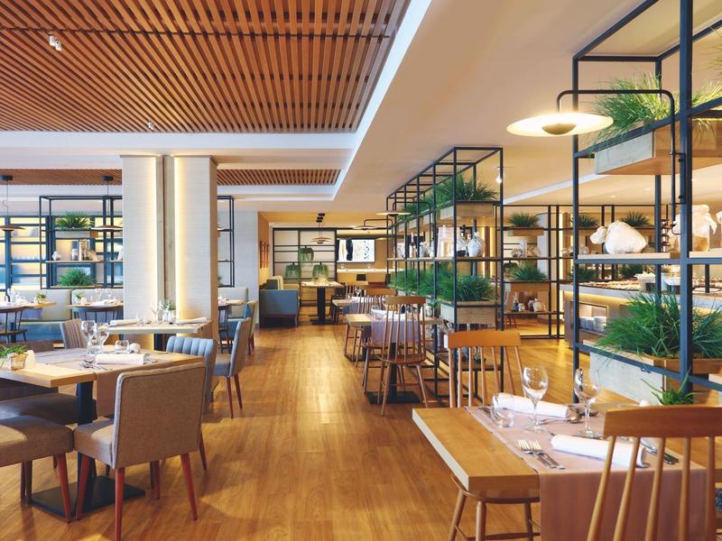 Modernes Restaurant mit Holzboden, gedeckten Tischen und grünen Pflanzen auf Metallregalen.