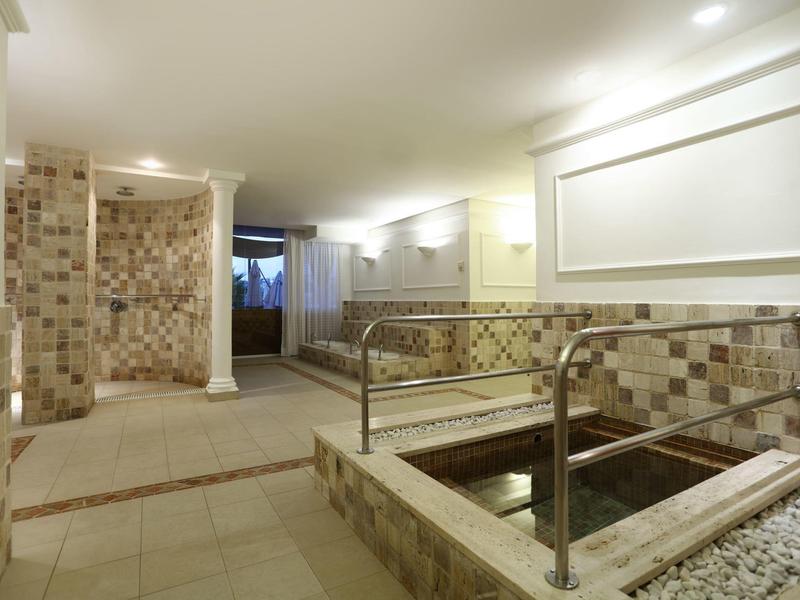 Innenraum eines Wellnessbereichs mit Whirlpool, Dusche, gepflasterten Wänden und warmem Licht.