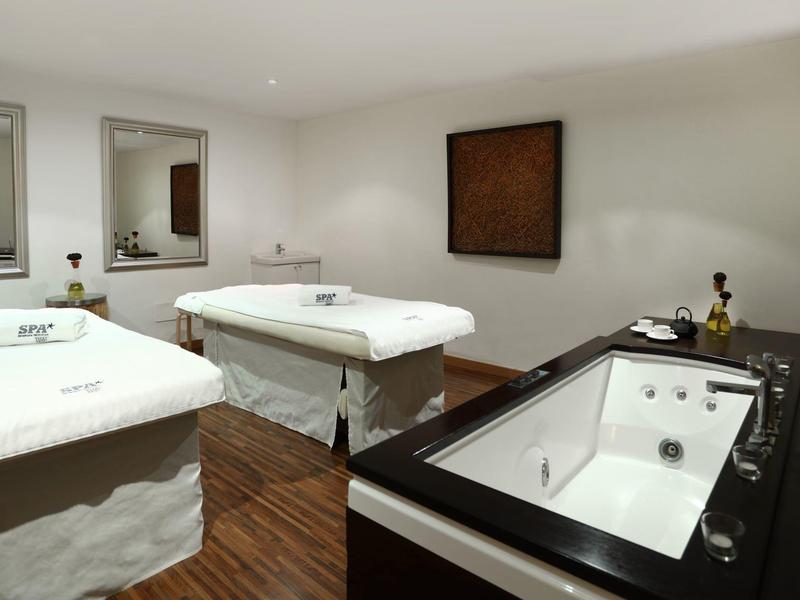 Moderner Spa-Raum mit zwei Massageliegen und einem großen Whirlpool, holzfarbener Boden.