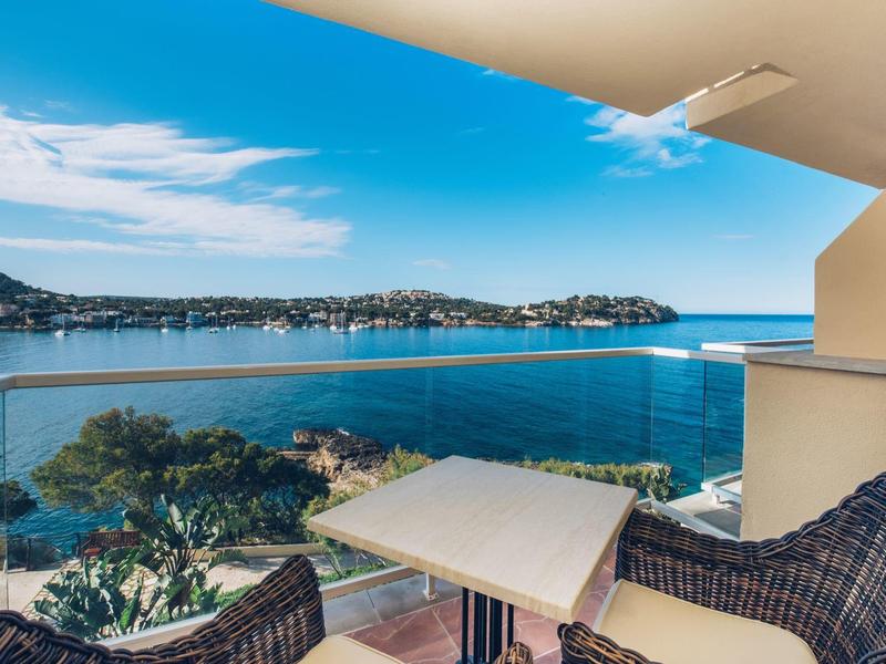Balkon mit Tisch und Stühlen, Glasgeländer, Blick auf Meer, Inseln und bewölkten blauen Himmel.