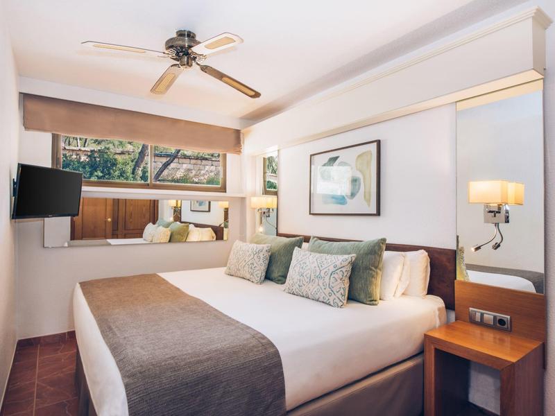 Gemütliches Schlafzimmer mit Doppelbett, Kissen, Deckenventilator und großem Fenster mit Blick.