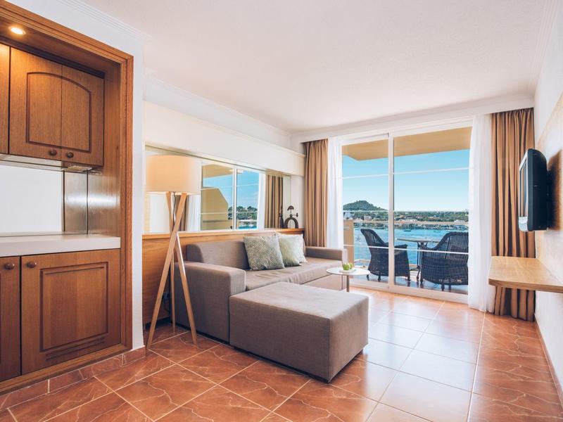 Helles Wohnzimmer mit grauem Sofa, Holzschränken und großer Glasschiebetür zum Balkon mit Meerblick.