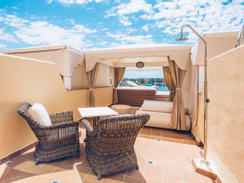 Gemütliche Dachterrasse mit Sitzgruppe, Pavillon, Sofa und Ausblick auf das Meer bei blauem Himmel.