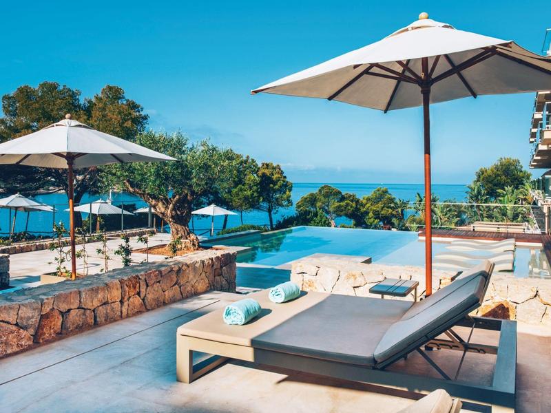 Moderner Poolbereich mit Liegestühlen, Sonnenschirmen und Meerblick bei klarem Himmel.