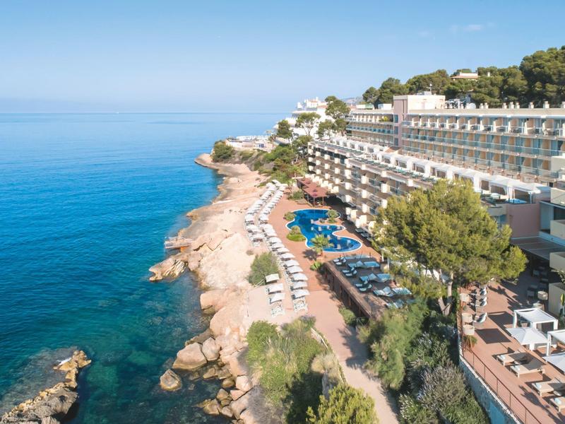 Hotelanlage am Felsenstrand mit Pool, Liegen und Aussicht auf das ruhige blaue Meer.
