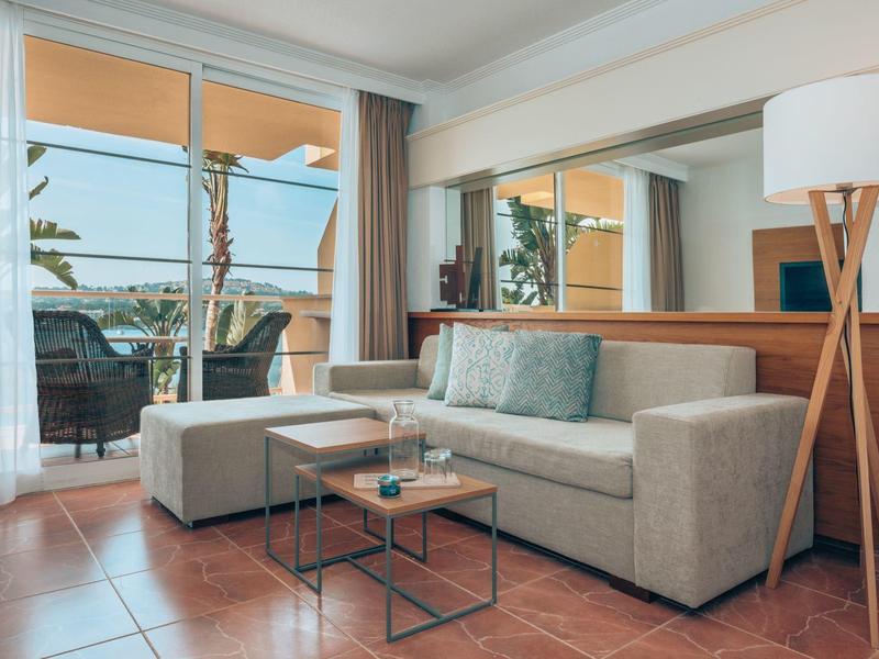 Modernes Wohnzimmer mit grauem Sofa, Glastisch, Stehlampe und Balkon mit Meerblick.