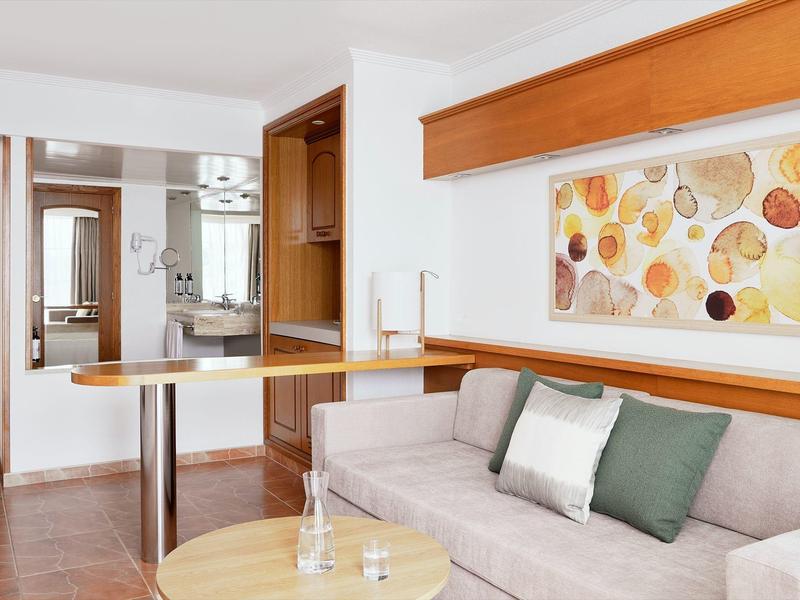 Wohnzimmer mit grauem Sofa, Holzmöbeln, hellem Wandbild und runder Glasvase auf Tisch.