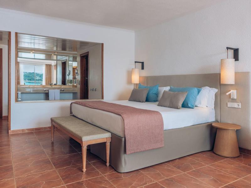 Hell eingerichtetes Schlafzimmer mit großem Bett, zwei Hängelampen, Holzboden und Fensterblick.