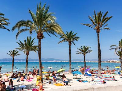 Strand mit vielen Menschen, blauer Himmel, türkisfarbenes Meer und hohe Palmen.