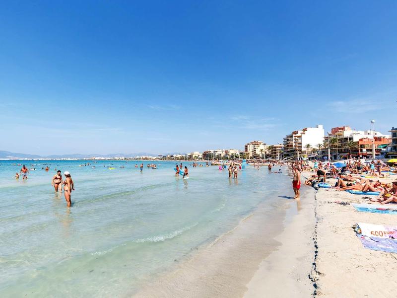 Strand mit klarem Wasser, blauem Himmel und vielen Sonnenbadenden an der Küste einer Stadt.