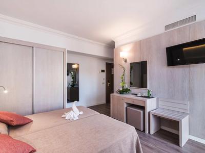 Modern hotel room with double bed, wall-mounted TV, and simple decor.