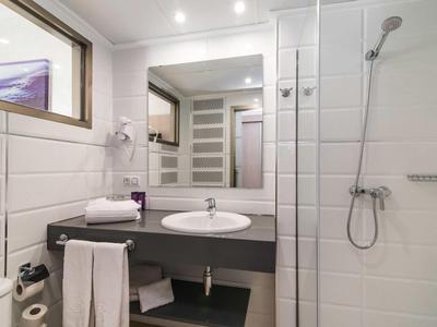 Modern hotel bathroom with white tiled walls, sink, and walk-in shower.