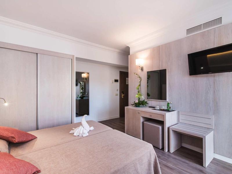 Modern hotel room with double bed, wall-mounted TV, and simple decor.