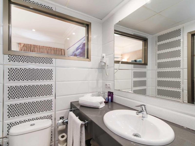 Modern bathroom with white wall tiles, large mirror, and sink on gray countertop.
