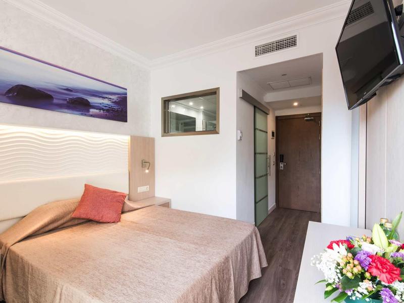 Bright hotel room with double bed, wall art, flat-screen TV, and flower arrangement.