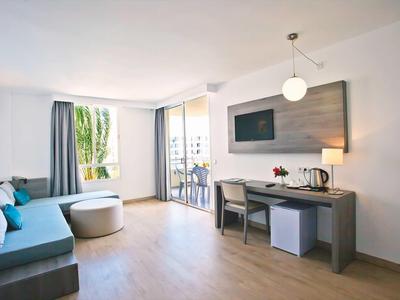 Chambre d'hôtel moderne avec canapé, bureau, télévision et balcon donnant sur la verdure.