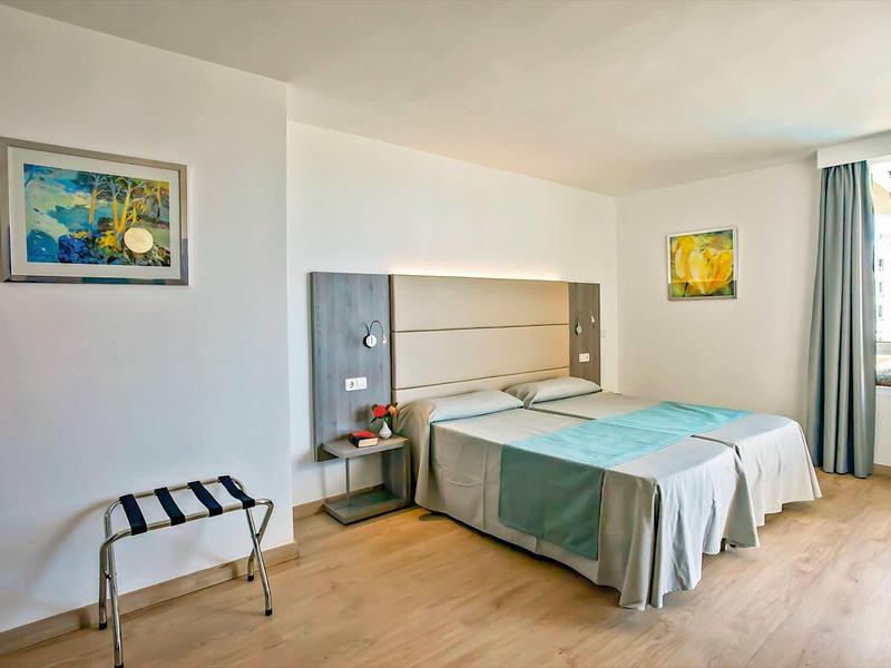 Chambre d'hôtel lumineuse avec lit double, fenêtre, chaise simple et œuvre murale.