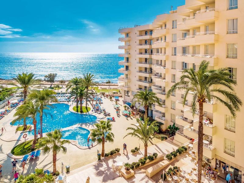 Complexe hôtelier avec piscine, palmiers et vue sur l'océan sous un ciel bleu